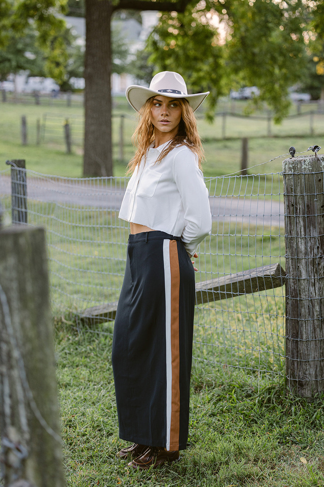 Woman in a white blouse and navy skirt with a stripe standing in a grassy field.