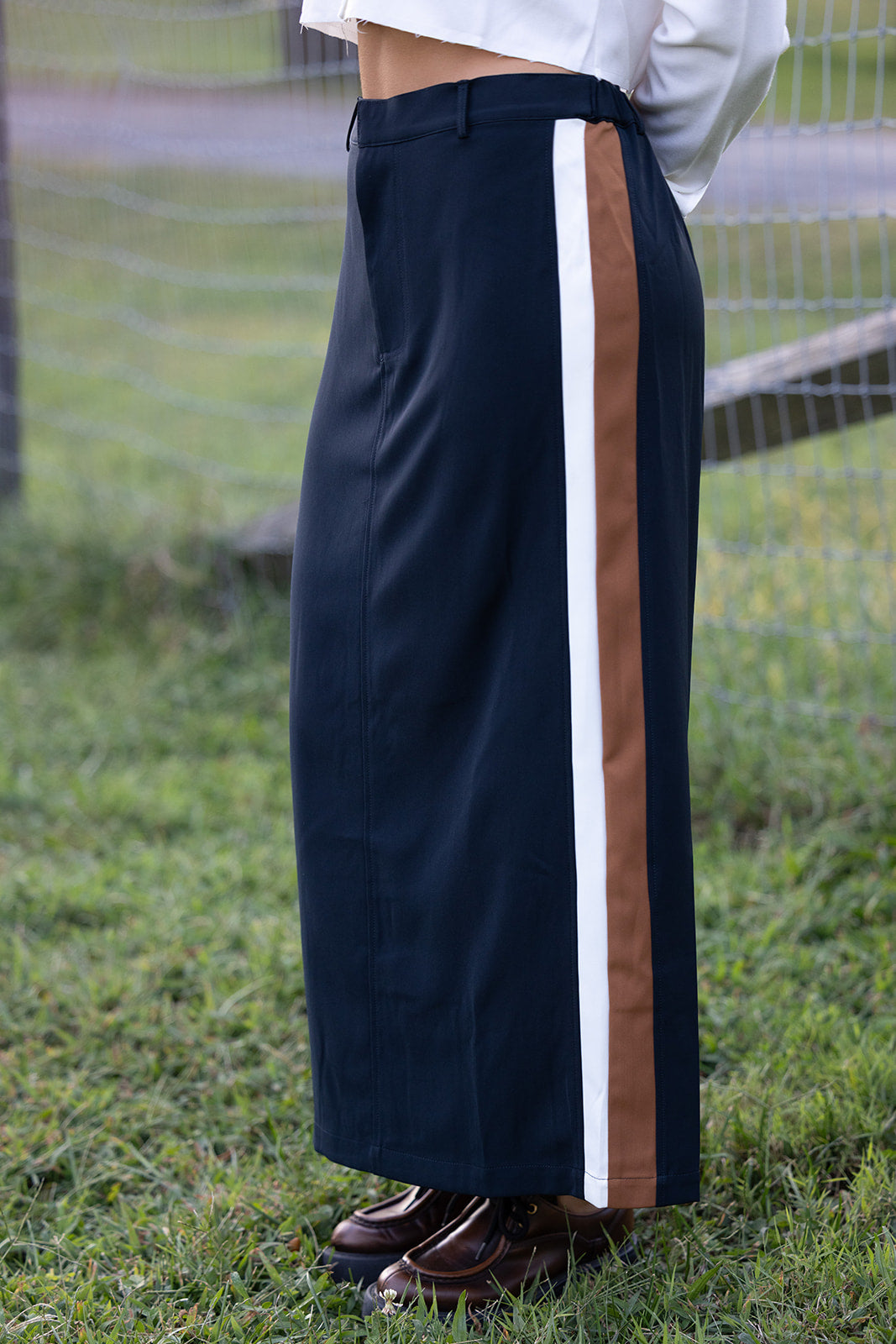 Woman in a navy maxi skirt with a stripe standing in a grassy field.