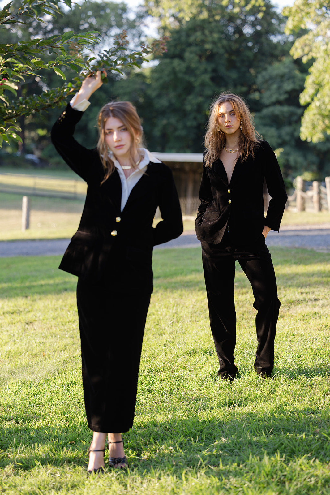 Two women in black velvet suits standing in a park with trees and grass in the background.