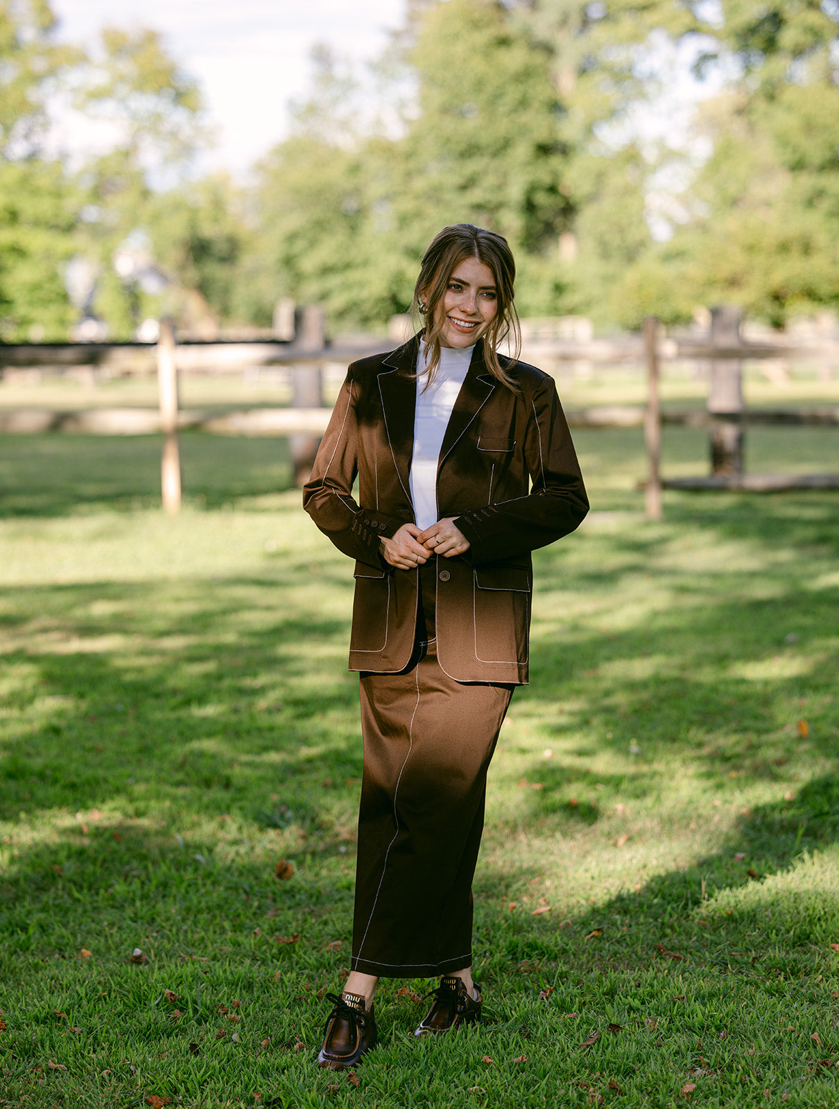 Woman in a brown stitching maxi skirt suit standing in a grassy field with trees in the background
