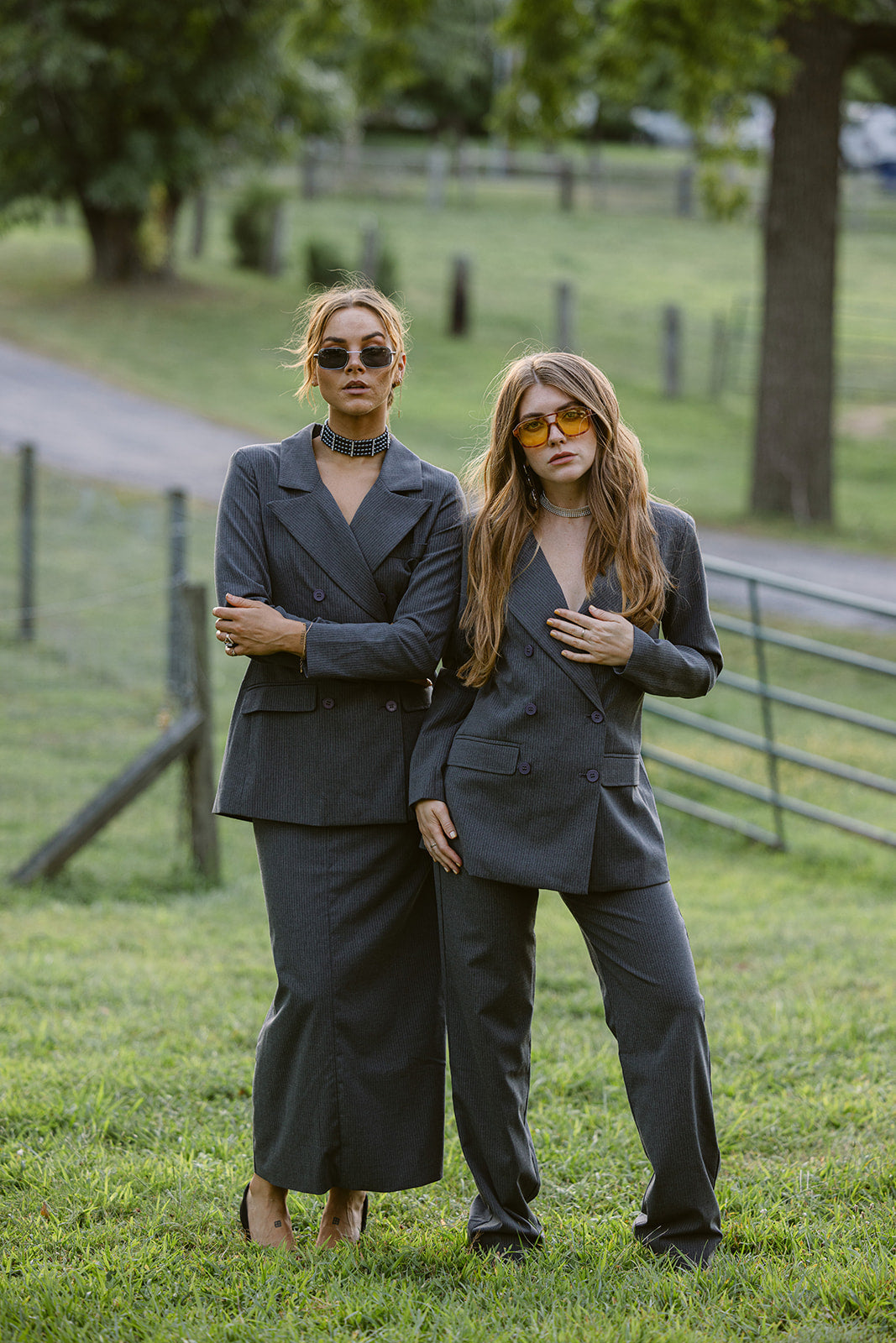 Two women in matching grey pinstripes suits standing in a grassy field.