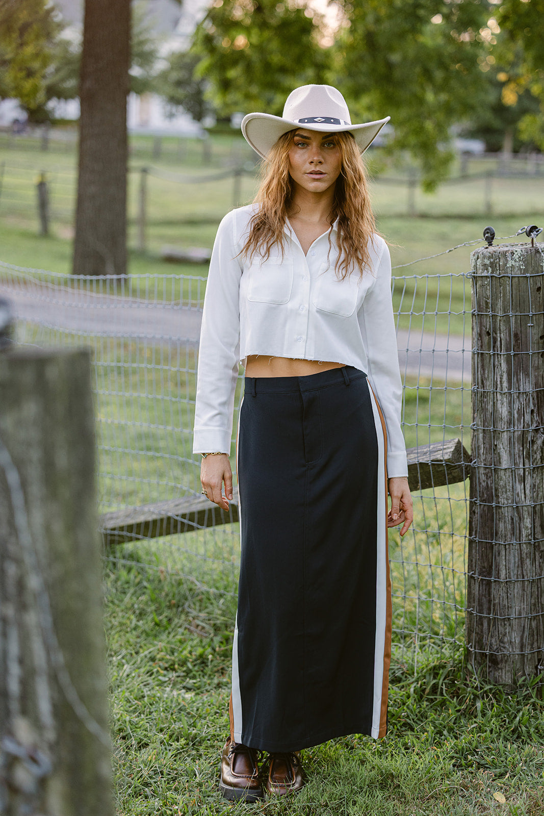 Woman in a white blouse and navy skirt with a stripe standing in a grassy field.